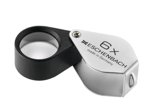 Small circular magnifier encased in black metal, with a silver coloured fold-out case with magnification written on case.