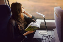 Load image into Gallery viewer, Woman using Daylight&#39;s Foldi Go on a train to read.
