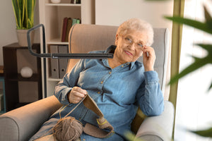 Woman sitting in an arm chair using the Electra lamp to knit.